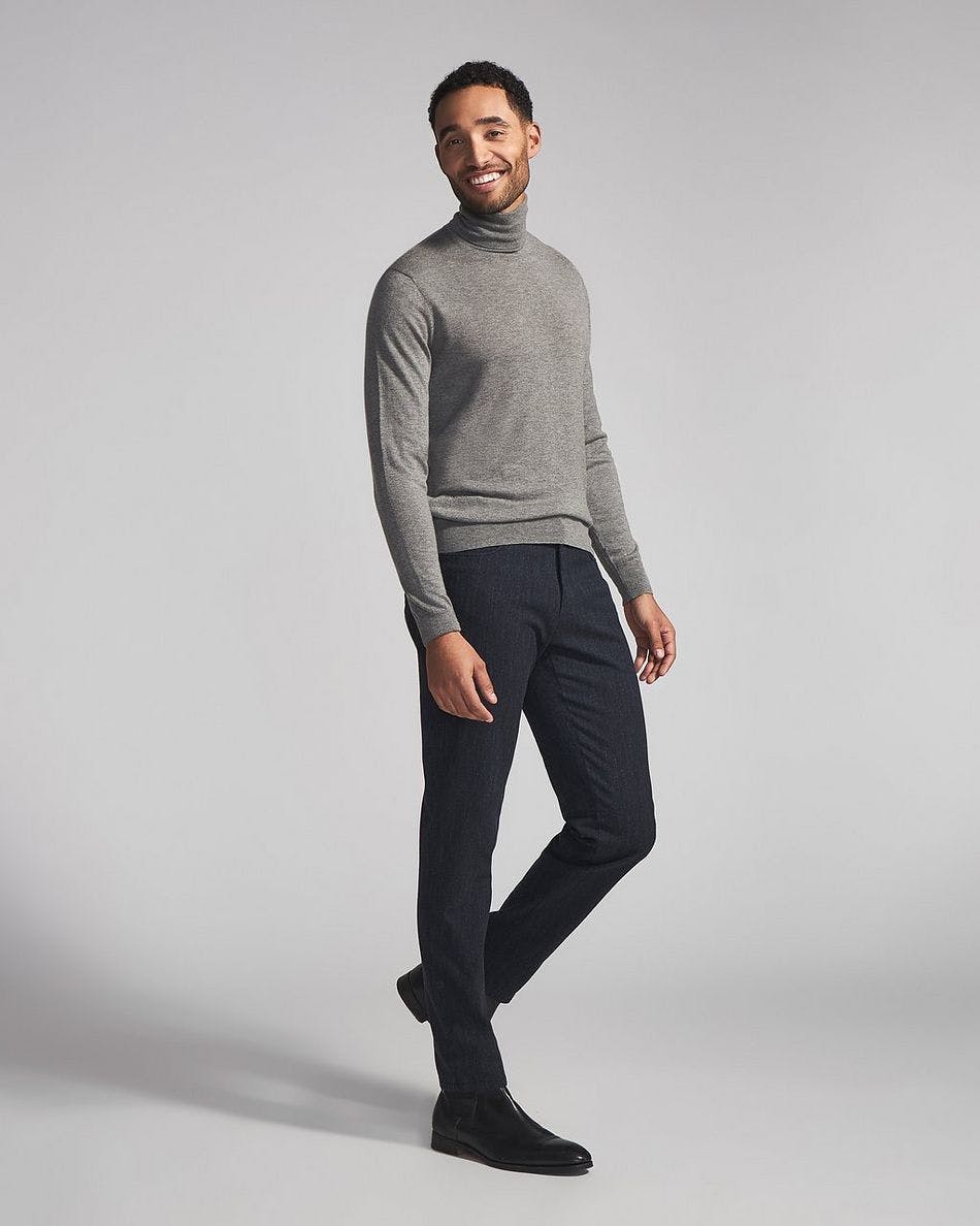 A man in a grey turtle neck sweater and black pants